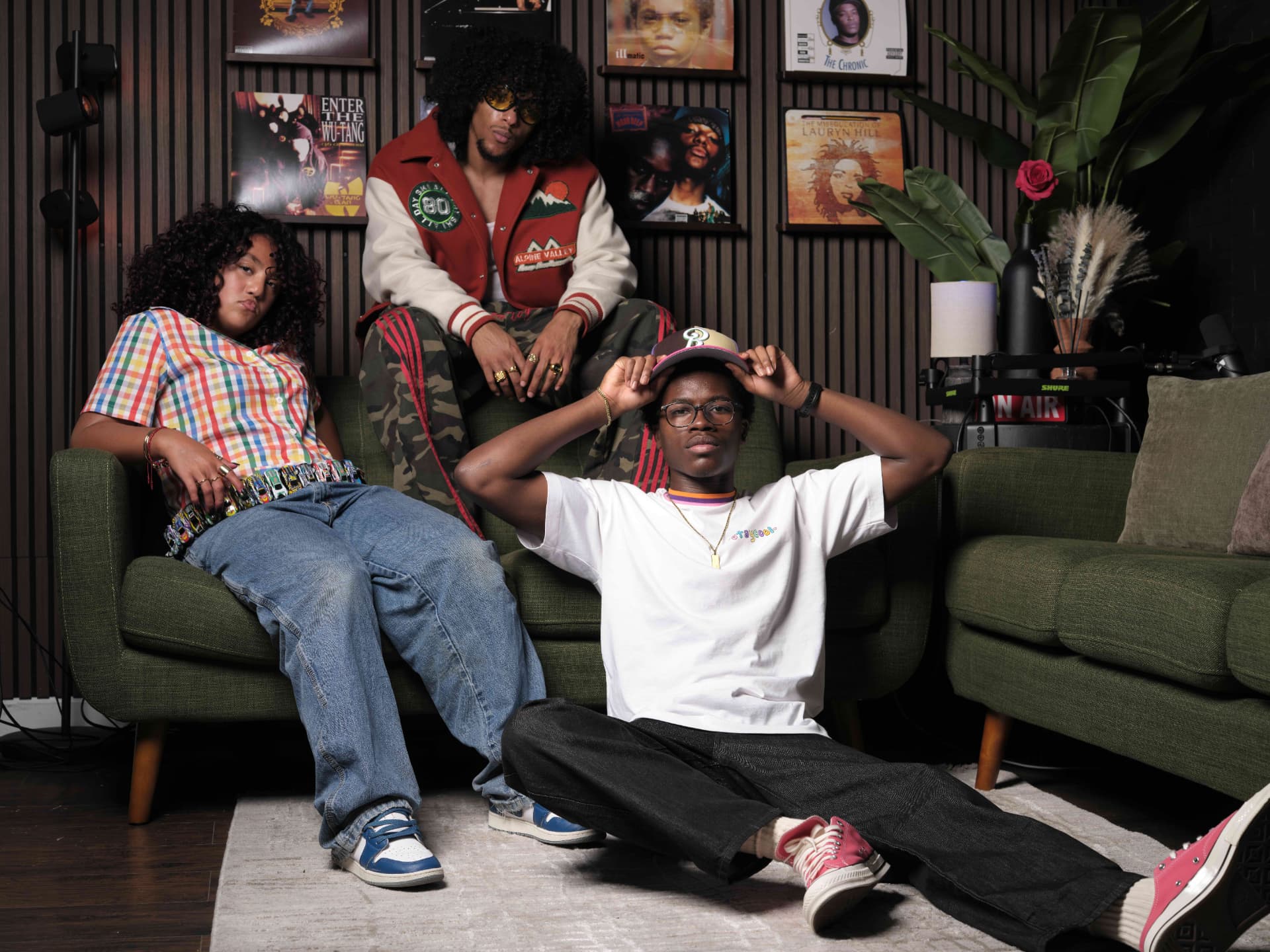 Three Beat The Odds participants relaxing on a sofa in a studio decorated with classic hip-hop album covers